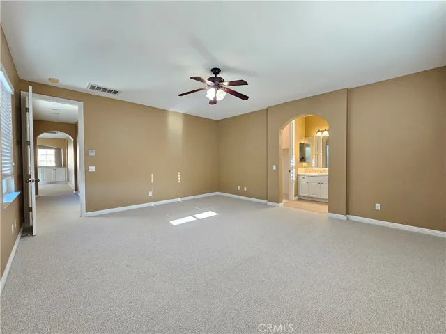 Luxurious southeast upstairs bedroom suite offering a private retreat. This generously sized space features a neutral color palette, plush carpeting, and a cooling ceiling fan. The suite includes an ample walk-in closet (or dressing area) with built-ins and direct access to a private en-suite bathroom with a spacious vanity. The elegant arched entryways add character, creating a tranquil and functional living area perfect for any homeowner.