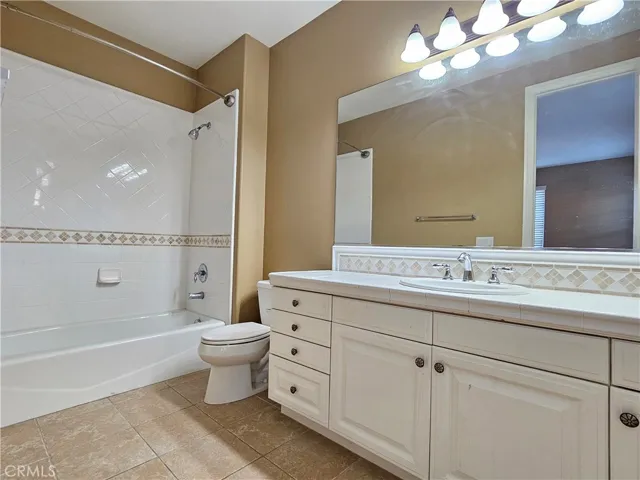 Northwest-facing upstairs full bathroom offering both function and style. Features a single vanity with ample white cabinetry for storage and a tiled countertop. The full-size tub/shower combo is surrounded by classic white tile with a decorative accent border. This bright space provides essential amenities in a clean, neutral environment.