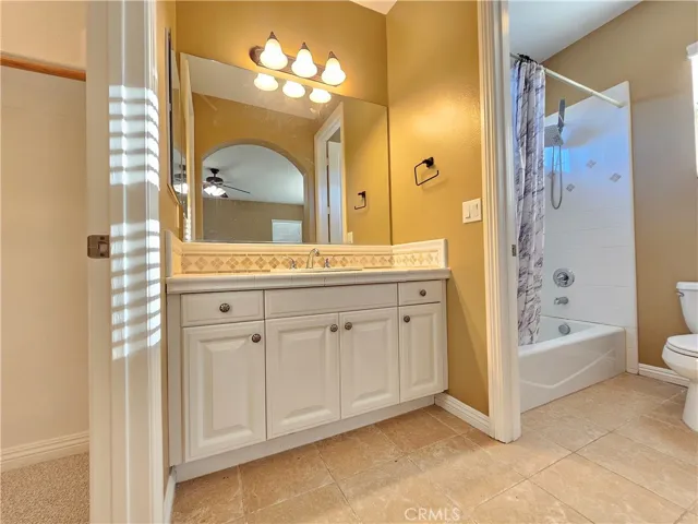Southeast upstairs en-suite full bathroom offering privacy and functionality for the primary suite. Features a single vanity with ample white cabinetry for storage and a tiled countertop. The full-size tub/shower combo is surrounded by classic white tile with a decorative accent border. This bright space provides essential amenities in a clean, neutral environment, with direct access to a nearby closet.