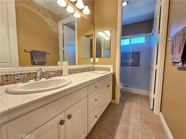 Northeast-facing upstairs full bathroom offering both function and style. Features a single vanity with ample white cabinetry for storage and a tiled countertop. The full-size tub/shower combo is surrounded by classic white tile with a decorative accent border.