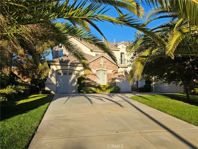 Front exterior view of the home featuring a wide concrete driveway, three car garage, stone and stucco façade, and mature landscaping with large palm trees framing the entry.