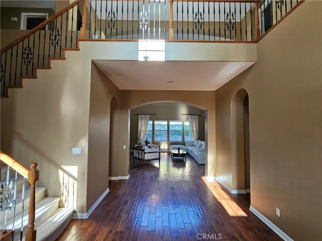Grand two-story entry and foyer featuring rich hardwood flooring, a dramatic staircase with wrought iron balusters, and a second-story balcony overlook. Wide arched entryways lead to the main living areas.