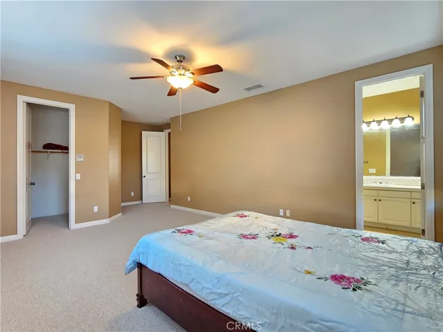 Stunning northwest upstairs bedroom suite offers a private retreat within the home. This light-filled space is generously sized, featuring a neutral color palette, plush carpeting, and a cooling ceiling fan. The suite includes a spacious walk-in closet with ample storage solutions, and direct access to a private en-suite bathroom with a large vanity. This versatile and inviting area is the perfect escape for relaxation and convenience.