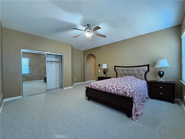 Expansive northeast upstairs bedroom offers both comfort and functionality. This light-filled space features a neutral color palette, plush carpeting, and a cooling ceiling fan. The large closet with mirrored sliding doors provides excellent storage, while the ample natural light from the window creates an inviting atmosphere.