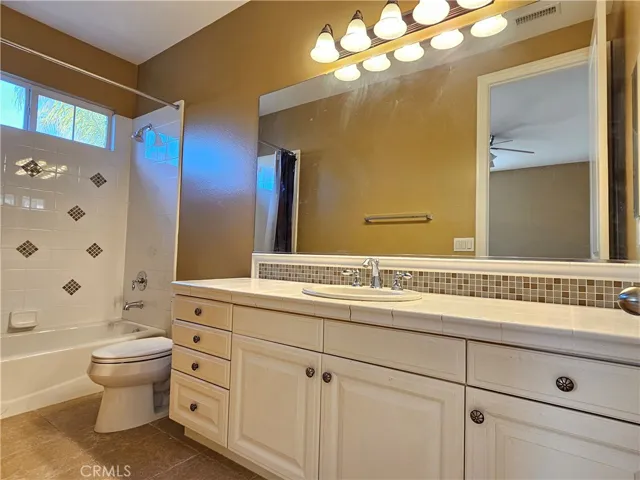 Southwest-facing upstairs full bathroom offers both convenience and style. Features a single vanity with ample storage provided by classic white cabinetry and solid-surface countertops. The full-size tub/shower combo is surrounded by white tile with a charming accent border. This bright space is completed by large mirrors and generous natural light, providing a clean and inviting atmosphere.
