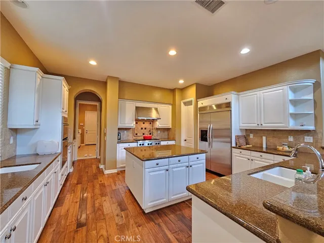 Stunning gourmet kitchen featuring crisp white cabinetry, luxurious granite countertops, and high-end stainless steel appliances. The heart of the home boasts a large central island with pendant lighting, perfect for entertaining or everyday meals. Includes a professional-grade gas range, built-in refrigerator, and ample storage space. The open floor plan and warm hardwood floors create an inviting atmosphere, with easy access to a nearby walk-in pantry and adjacent rooms.