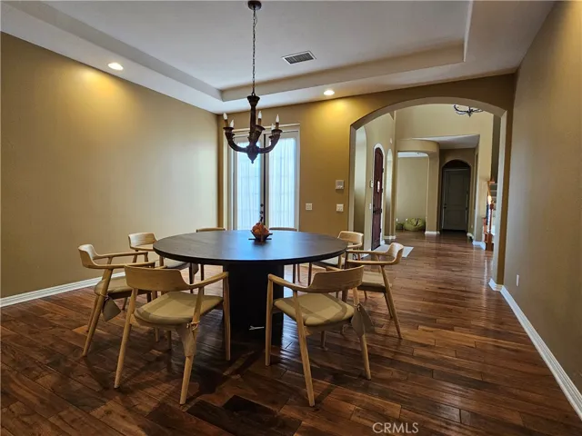 Elegant Dining Room offering a seamless transition to the main hall through a wide arched entryway. The space is filled with natural light from the main entrance door, highlighting the warm wall tones and dark wood flooring.