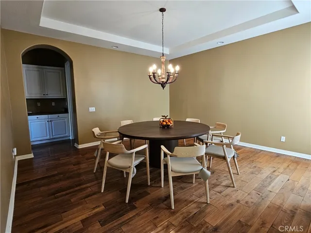 Formal Dining Room featuring rich hardwood flooring and an elegant chandelier. Note the tray ceiling and arched entry to the dining cabinet.