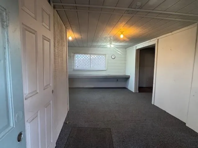 Hall featuring dark colored carpet and wood ceiling