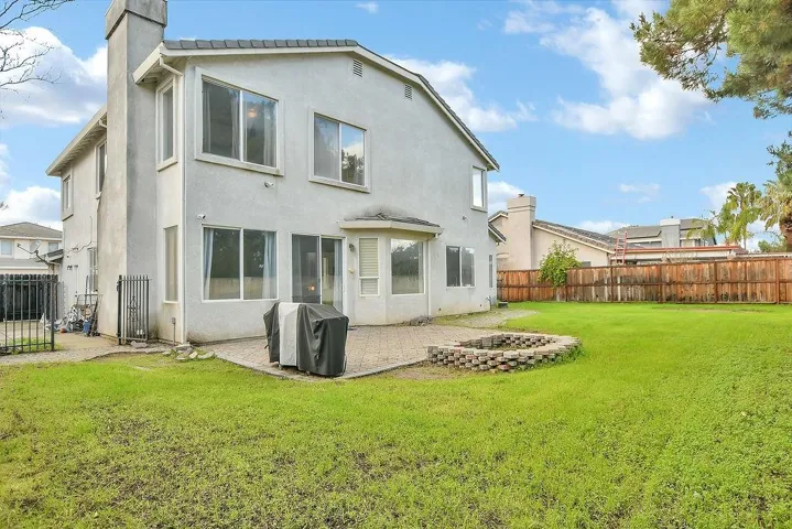 Rear view of property with stucco siding, a fenced backyard, a chimney, a patio, and a fire pit