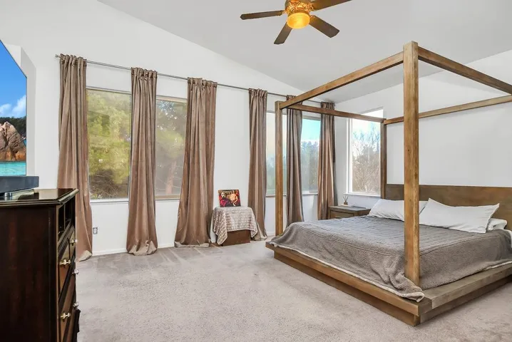 Carpeted bedroom featuring lofted ceiling, a ceiling fan, and multiple windows