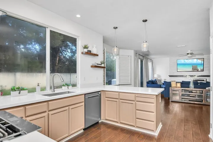 Kitchen with dark wood-style flooring, light brown cabinetry, hanging light fixtures, and stainless steel appliances