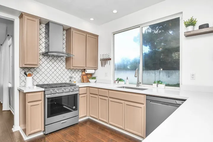 Kitchen with stainless steel appliances, wall chimney exhaust hood, dark wood-style floors, light brown cabinets, and recessed lighting