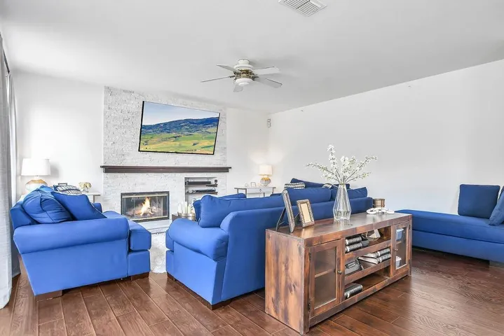 Living area featuring dark wood finished floors, a ceiling fan, and a stone fireplace