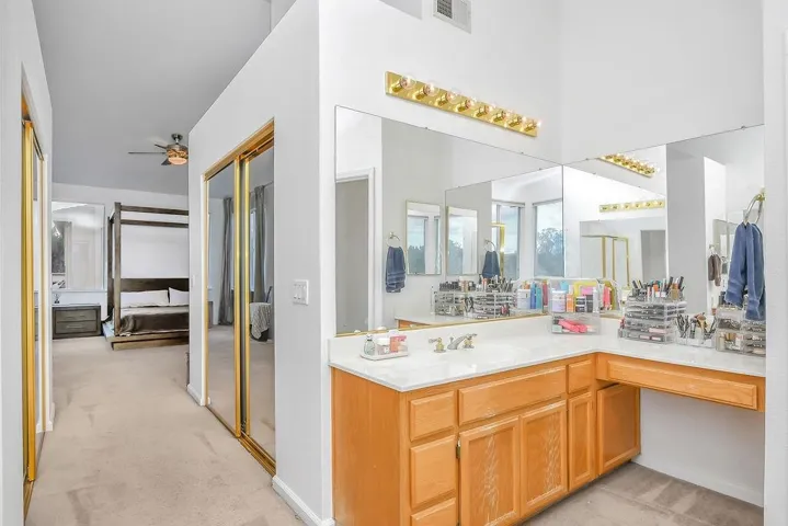 Ensuite bathroom featuring light carpet, vanity, and a ceiling fan
