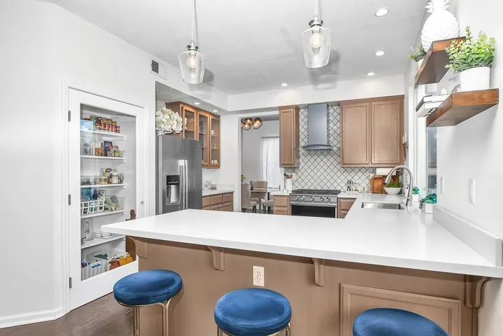 Kitchen with open shelves, a breakfast bar, stainless steel appliances, a peninsula, and light countertops