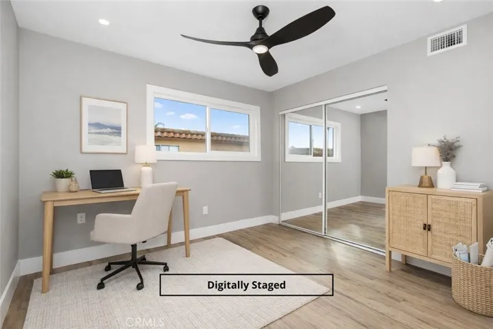 Digitally staged bedroom featuring mirrored closet doors, modern ceiling fan, and space for a home office.