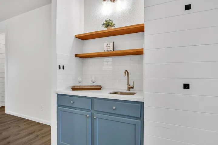 Bar with blue cabinetry, open shelves, light stone counters, and wood finished floors