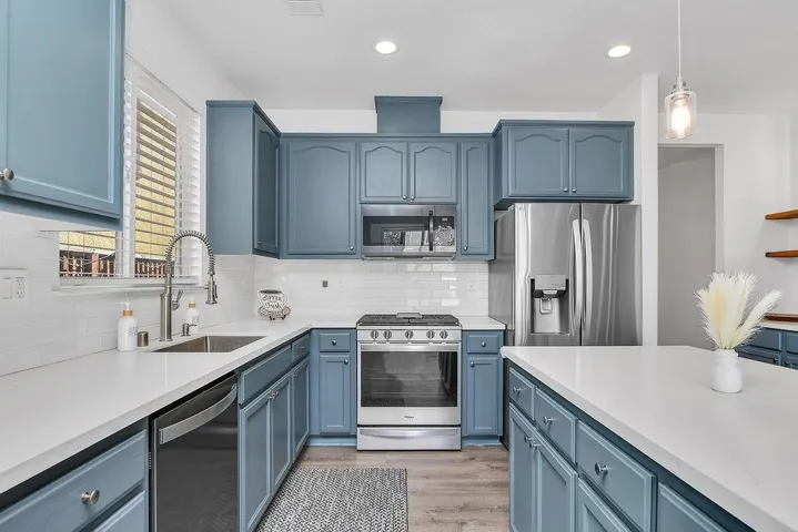 Kitchen featuring blue cabinetry, stainless steel appliances, light wood-style floors, backsplash, and recessed lighting