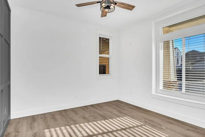 Empty room with crown molding, wood finished floors, and a ceiling fan