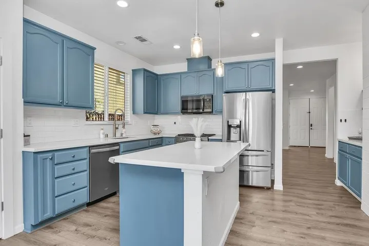 Kitchen featuring blue cabinets, stainless steel appliances, pendant lighting, a kitchen island, and backsplash