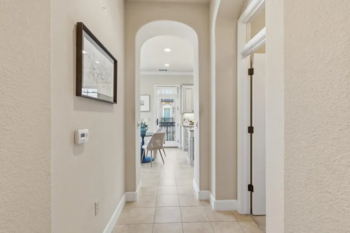 Hallway featuring arched walkways, light tile patterned floors, a textured wall, and ornamental molding