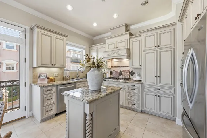 Kitchen with crown molding, appliances with stainless steel finishes, light stone counters, cream cabinets, and light tile patterned floors