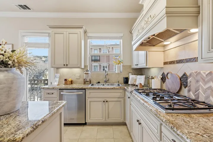Kitchen featuring appliances with stainless steel finishes, custom range hood, light stone counters, plenty of natural light, and crown molding