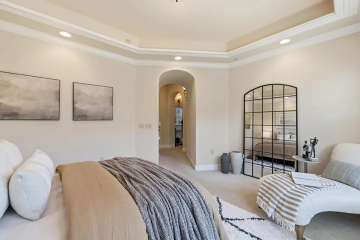 Carpeted bedroom featuring arched walkways, a raised ceiling, crown molding, and recessed lighting