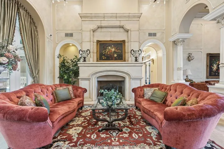 Sitting room with a towering ceiling, a fireplace, arched walkways, and ornate columns