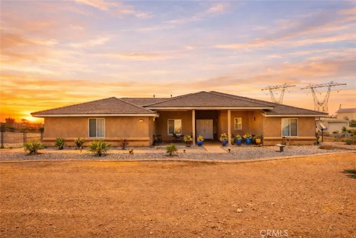 Beautiful single-story desert home set against a stunning sunset sky, featuring warm stucco and clean, low-maintenance landscaping on a spacious lot with wide open views.
