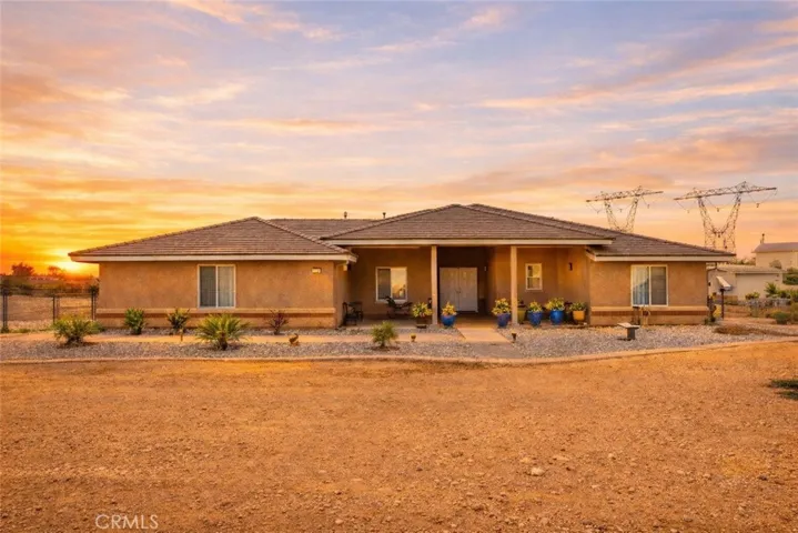 Beautiful single-story desert home set against a stunning sunset sky, featuring warm stucco and clean, low-maintenance landscaping on a spacious lot with wide open views.