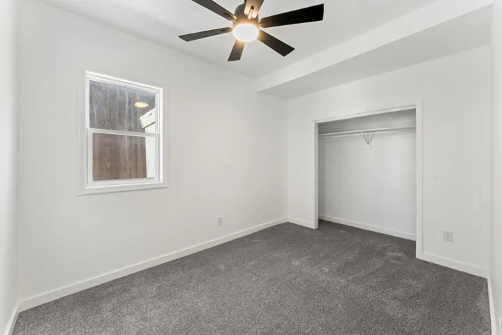 Unfurnished bedroom featuring dark colored carpet, a closet, and ceiling fan