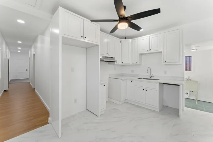 Kitchen with light marble finish floors, light countertops, white cabinetry, under cabinet range hood, and recessed lighting