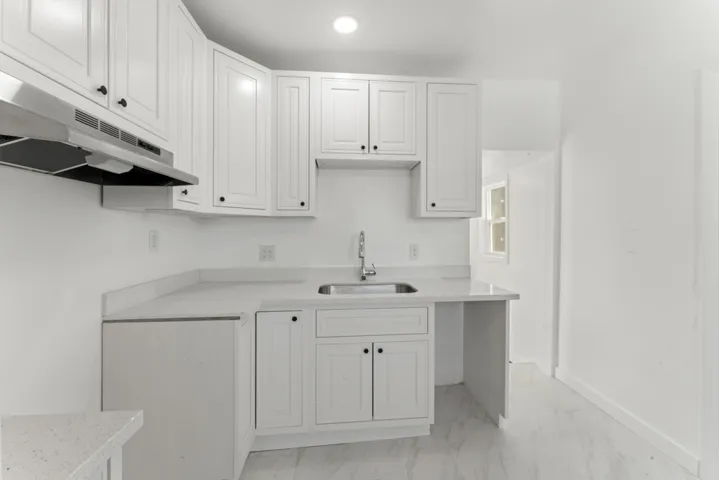 Kitchen with light marble finish flooring, white cabinetry, and under cabinet range hood