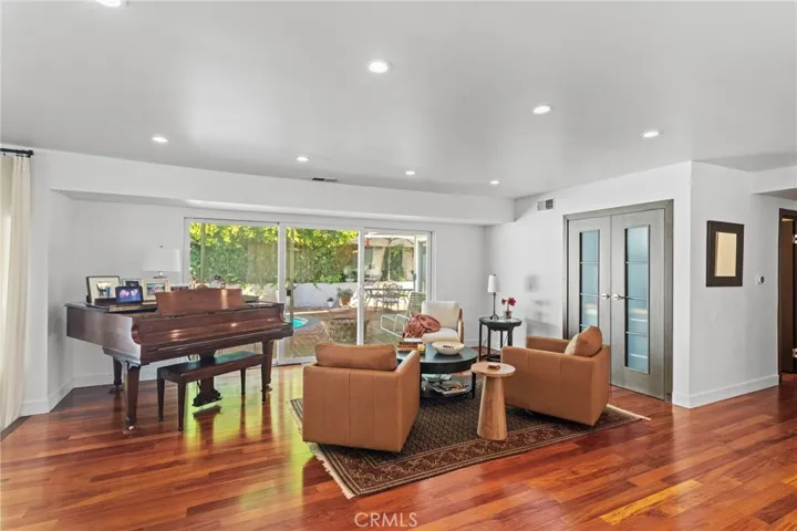 Family Den area - features baby grand piano, custom double doors that exit to the outdoor living area, and views of the pool/patio and manicured hedging providing privacy.