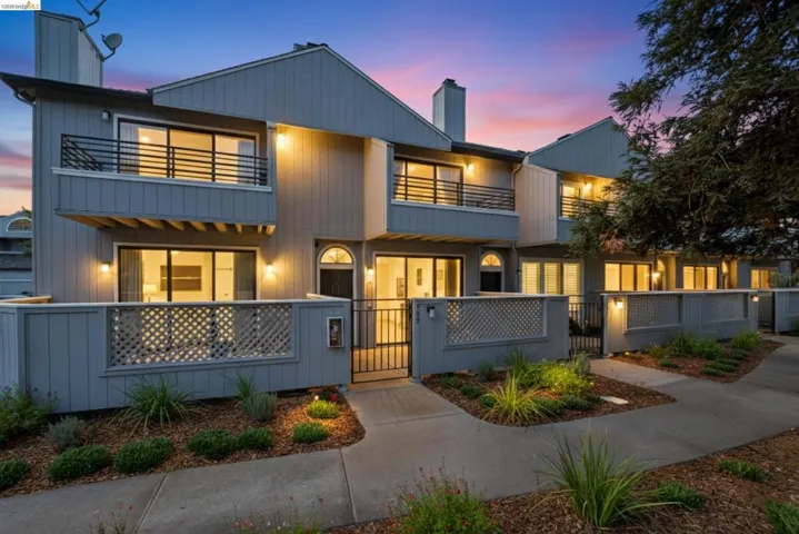 Modern home featuring a chimney, a gate, a fenced front yard, and a balcony