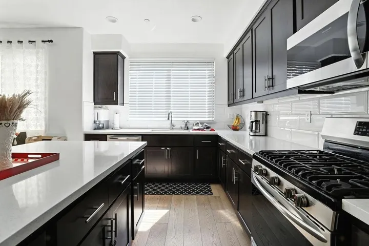 Kitchen featuring dark cabinets, stainless steel appliances, light wood-style floors, light stone countertops, and backsplash