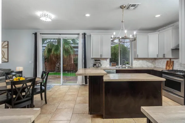 Kitchen featuring stainless steel gas stove, pendant lighting, white cabinets, a chandelier, and a kitchen island