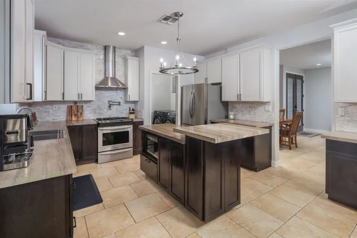 Kitchen featuring dark brown cabinets, wood counters, appliances with stainless steel finishes, hanging light fixtures, and tasteful backsplash
