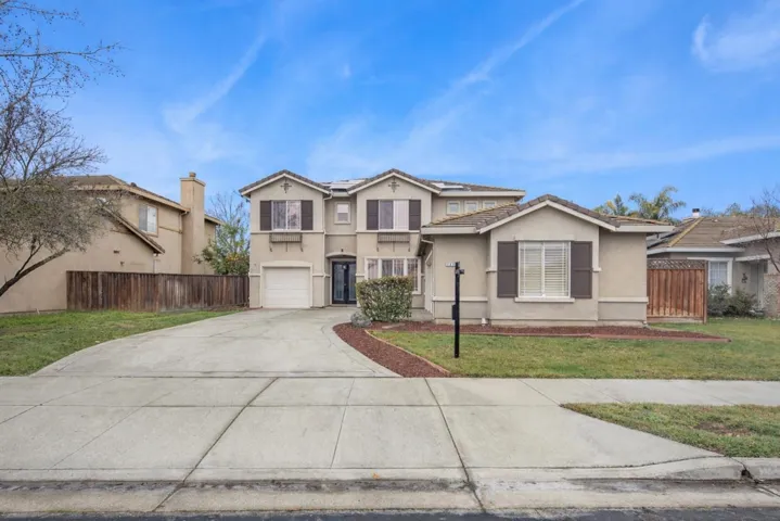 Traditional home featuring driveway, stucco siding, solar panels, and an attached garage