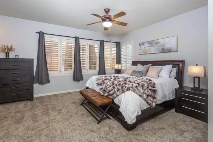 Carpeted bedroom with multiple windows and a ceiling fan