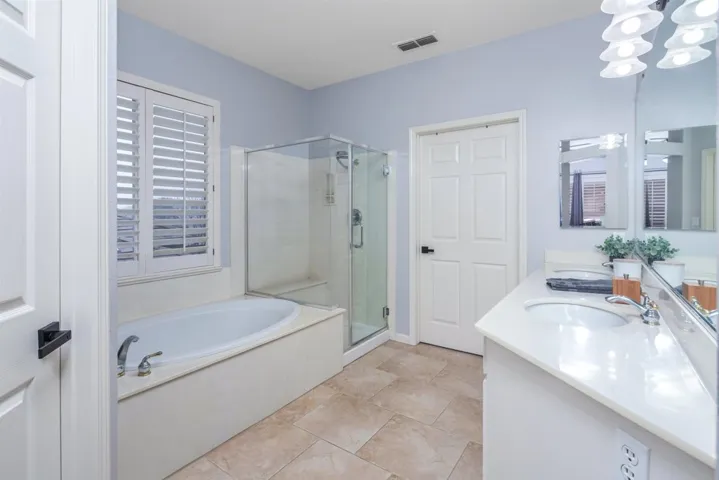 Full bath with a shower stall, double vanity, a garden tub, and a chandelier