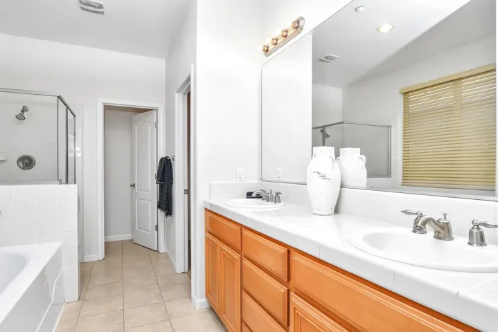 Full bathroom featuring a shower stall, a garden tub, double vanity, and light tile patterned floors