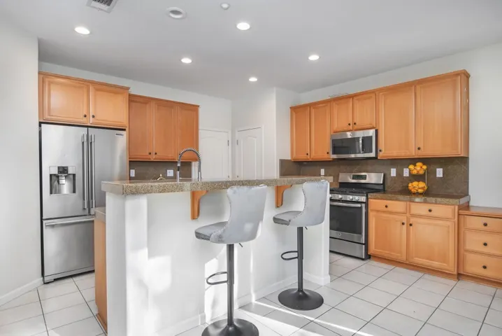 Kitchen with a breakfast bar, stainless steel appliances, light tile patterned flooring, a center island with sink, and recessed lighting
