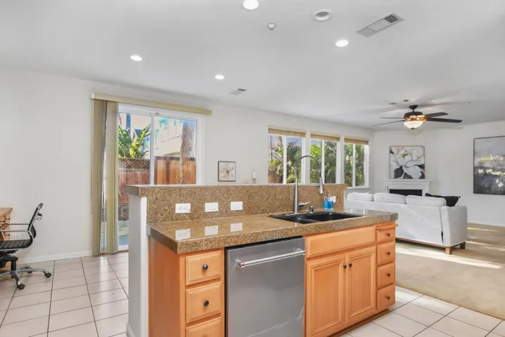 Kitchen with an island with sink, stainless steel dishwasher, light tile patterned floors, a fireplace, and light brown cabinetry