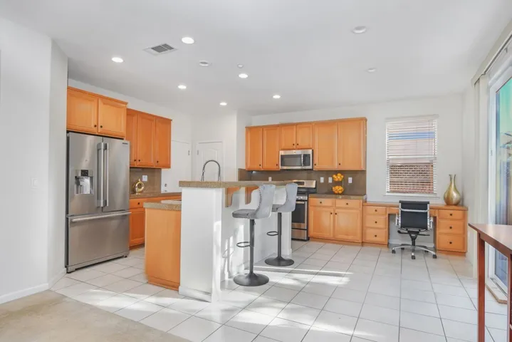 Kitchen with a breakfast bar, appliances with stainless steel finishes, light tile patterned floors, recessed lighting, and a kitchen island with sink