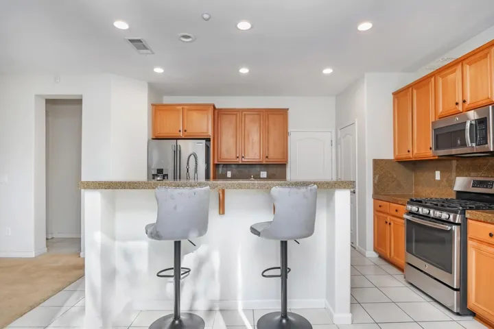 Kitchen featuring a breakfast bar, appliances with stainless steel finishes, decorative backsplash, light tile patterned floors, and recessed lighting