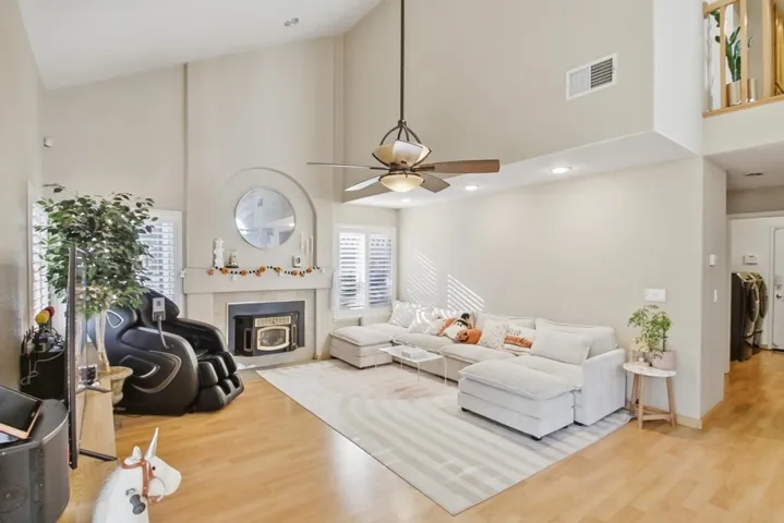 Living room featuring high vaulted ceiling, light wood-style floors, a glass covered fireplace, washing machine and dryer, and a ceiling fan