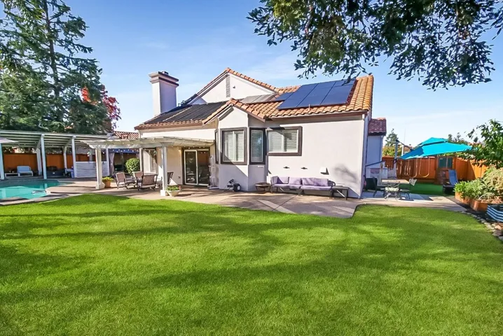Rear view of property featuring a patio area, a fenced backyard, an outdoor hangout area, stucco siding, and solar panels